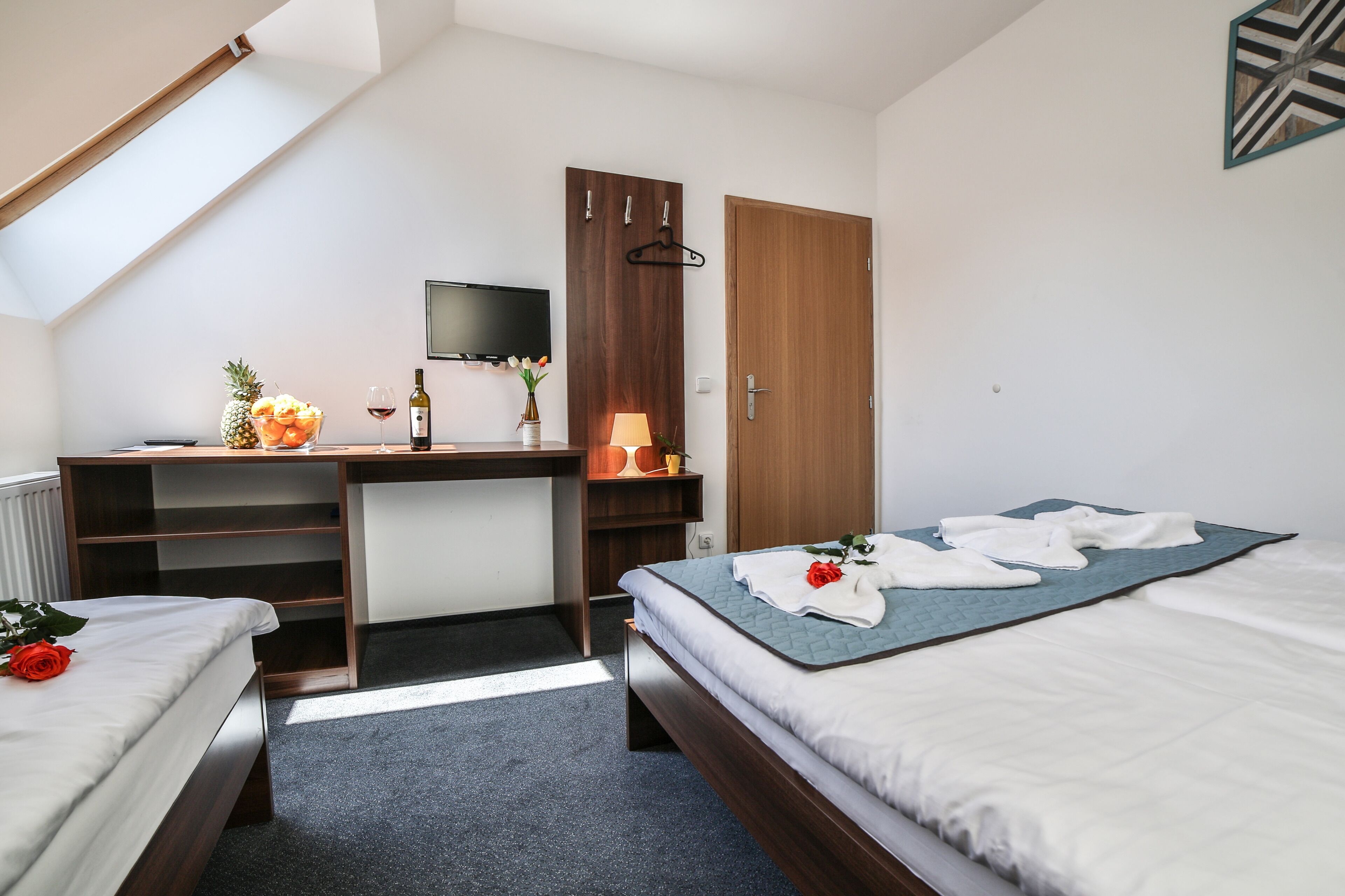 A hotel room with two beds, a desk, a TV, and a wooden wardrobe.
