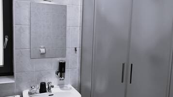 Une salle de bain avec un lavabo blanc, un miroir, une serviette, une douche et des toilettes.