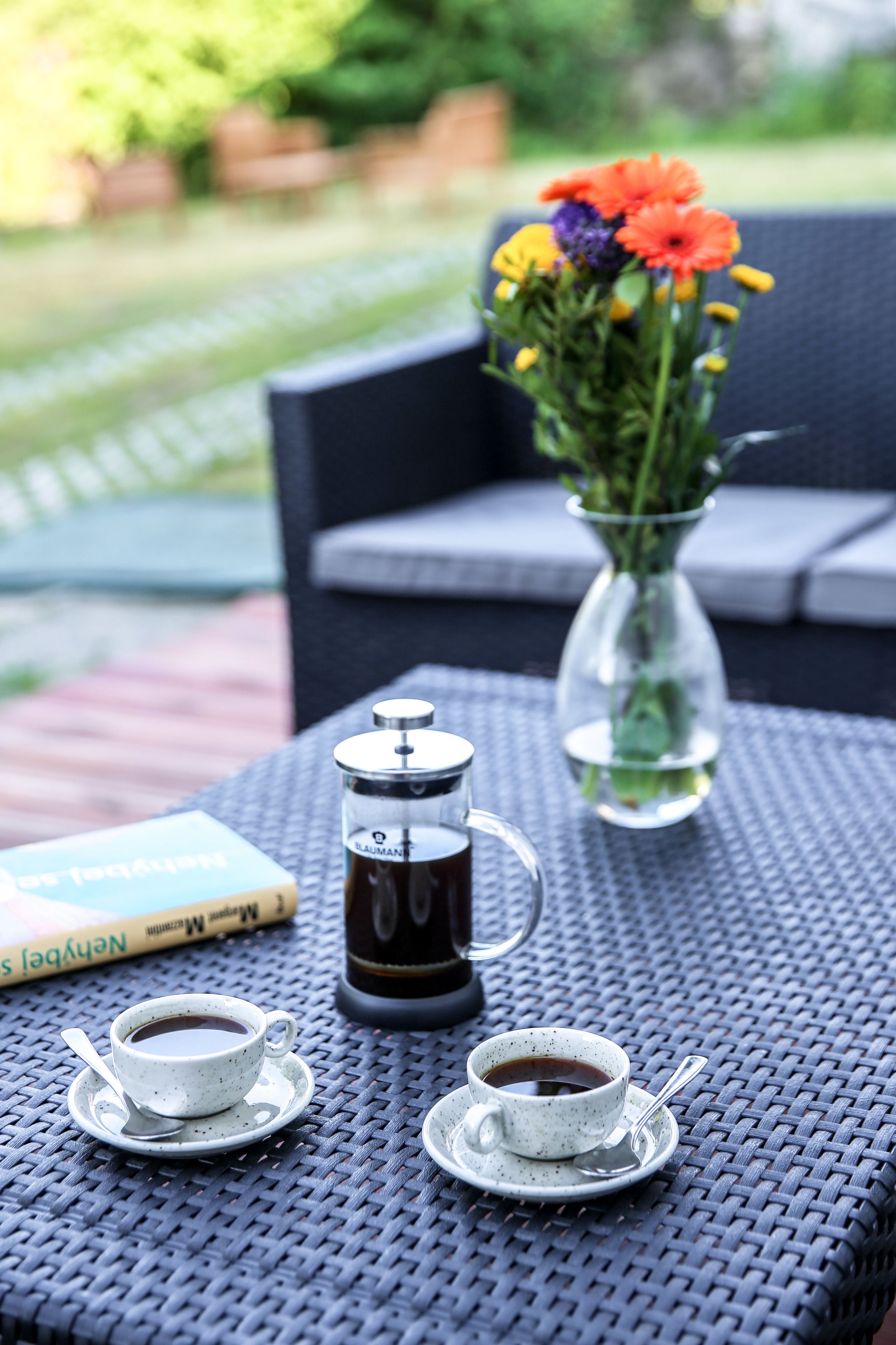 Une table avec deux tasses de café, une cafetière à piston et un vase rempli de fleurs.