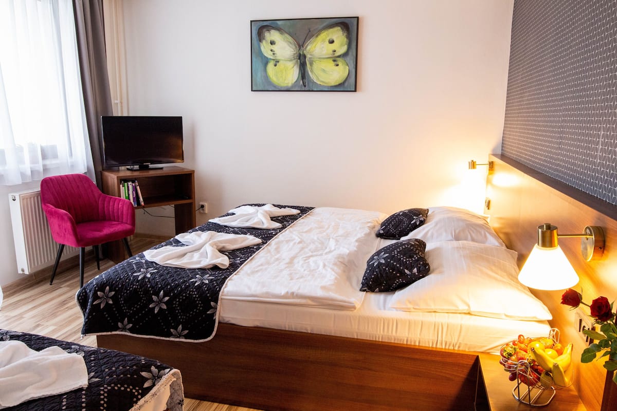 A hotel room with a bed, a TV, a red chair, and a wall-mounted artwork.