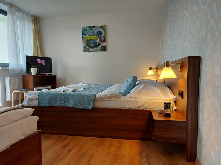 Een netjes opgemaakt bed met een blauwe quilt, een bedlampje en een klein tafeltje met een kopje en een boek.