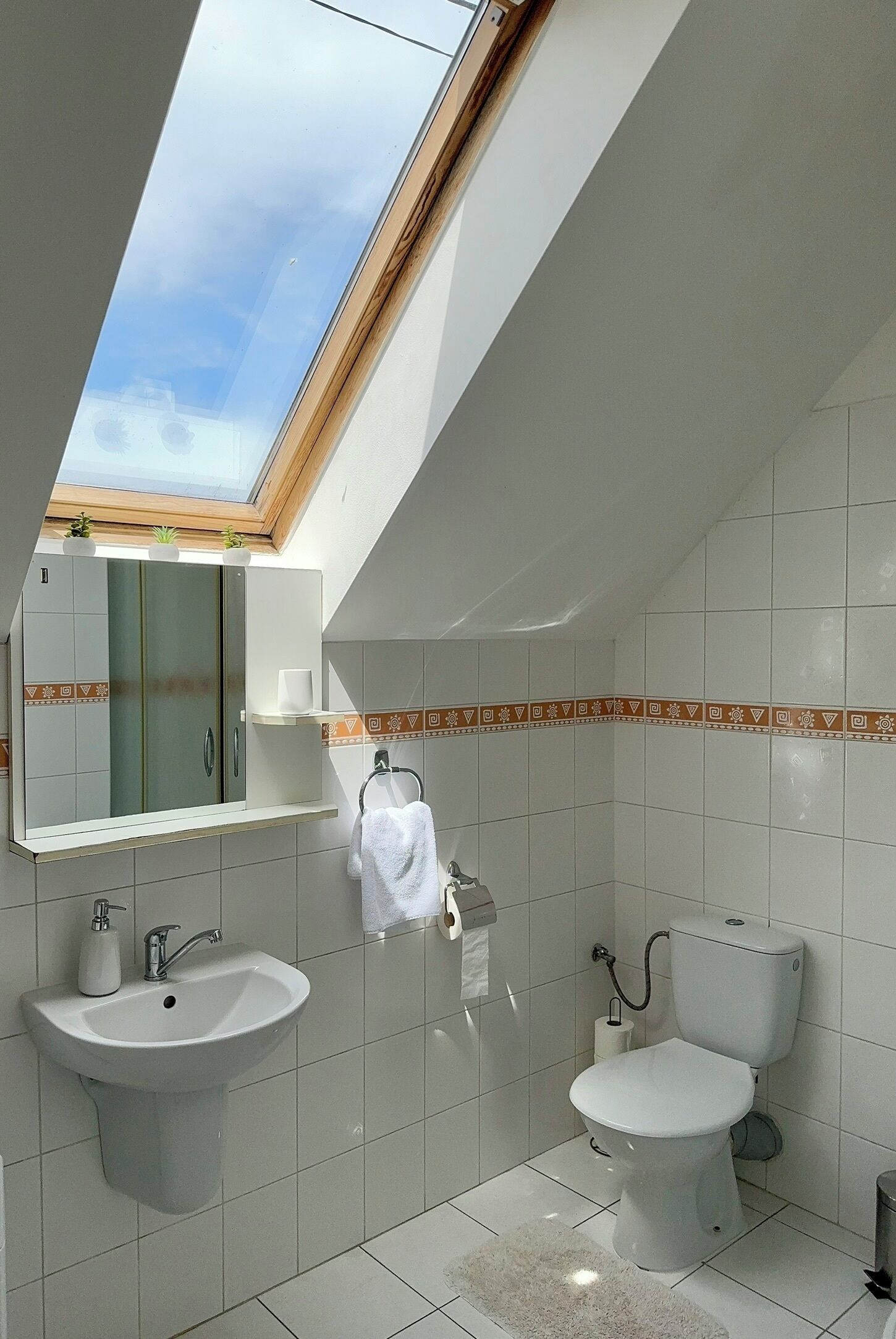 Un baño moderno con tragaluz, lavamanos, inodoro y espejo.