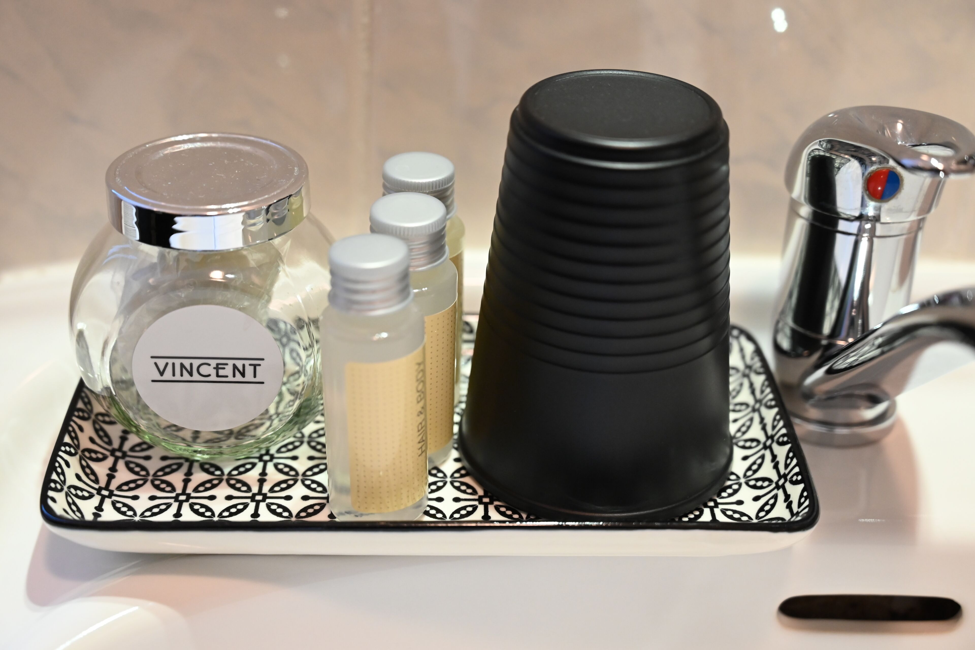 A bathroom sink area with a black soap dispenser, a bottle labeled "VINCENT," and two smaller bottles.