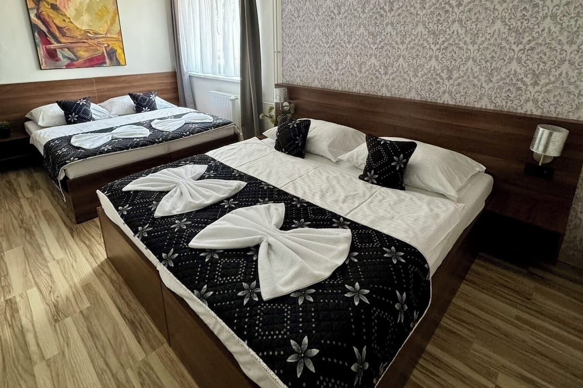 A hotel room with two beds, a large painting on the wall, a patterned wallpaper, and a wooden floor.