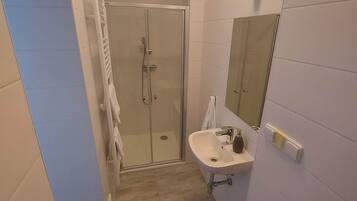 A narrow bathroom with a glass-enclosed shower, a white sink, and a mirror on the wall.