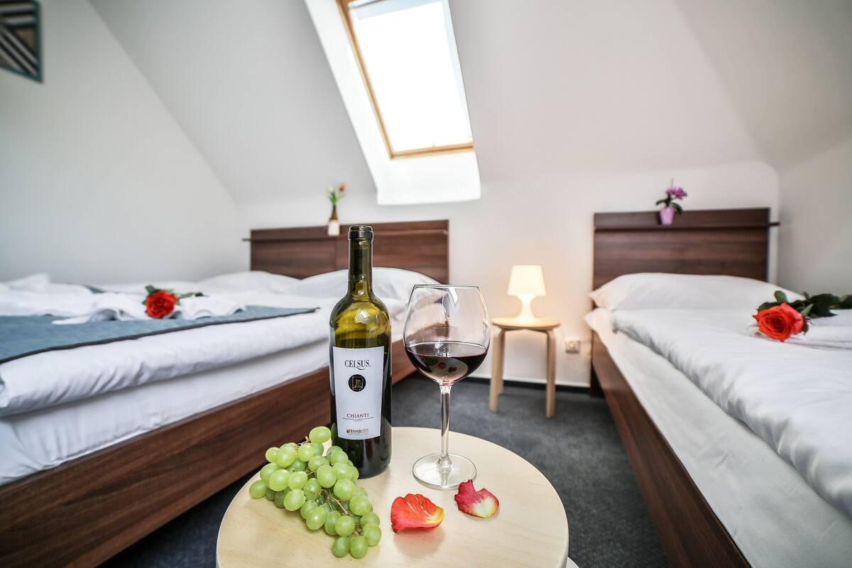A hotel room with two beds, a round table with a bottle of wine, a glass of wine, and some fruit.