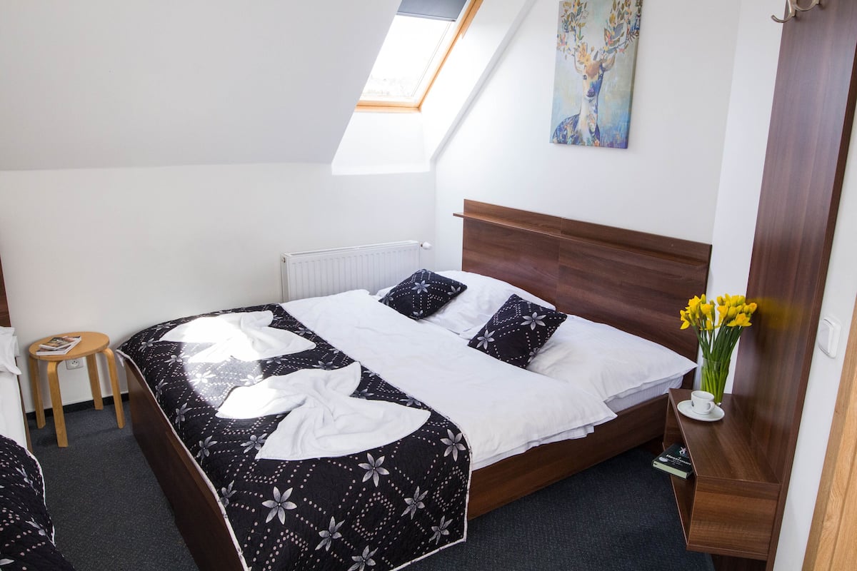 A neatly made bed with a black and white floral bedspread, a wooden headboard, and a small bedside table with a cup and book.