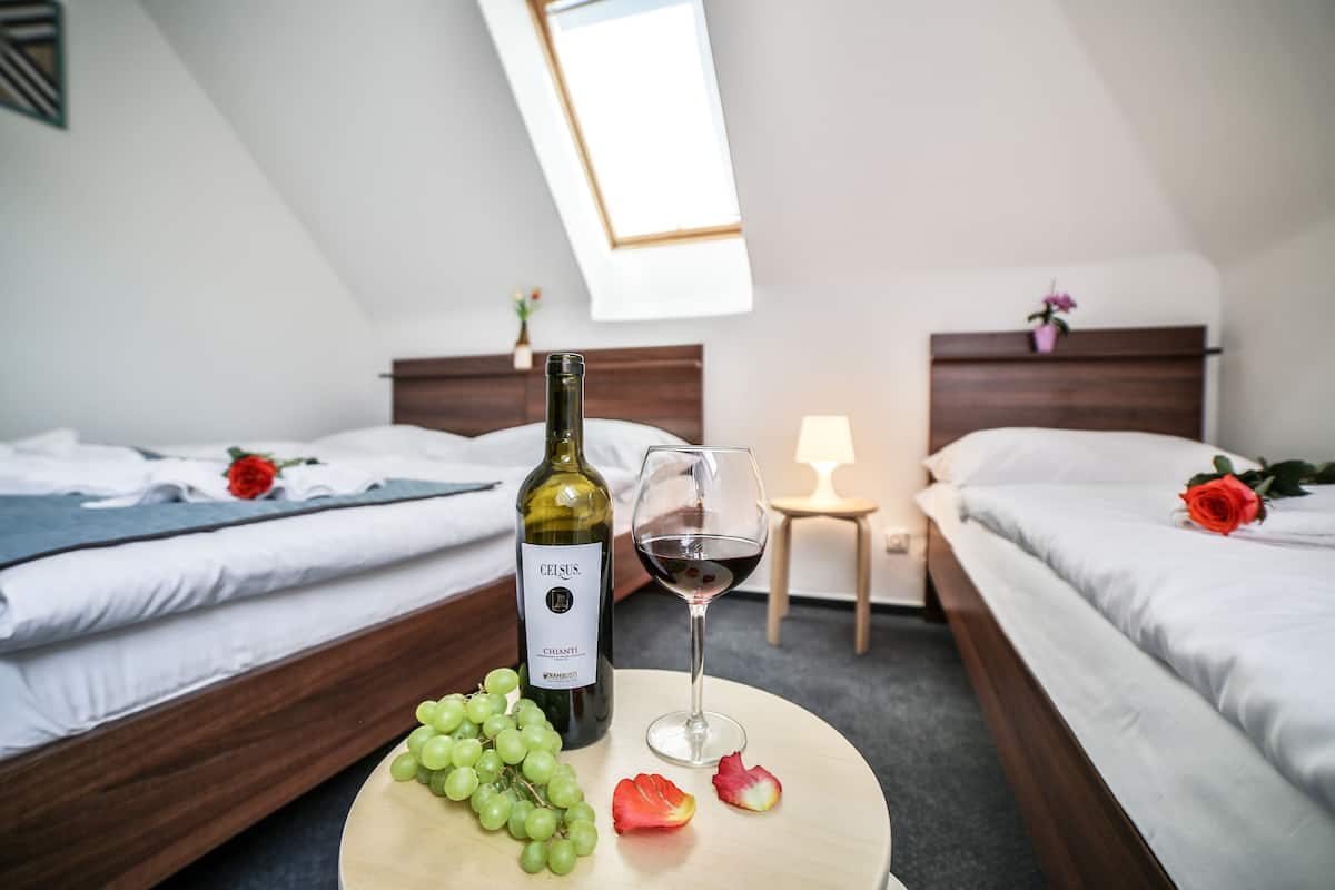 A hotel room with two beds, a round table with a bottle of wine, a glass of wine, and a bunch of grapes.