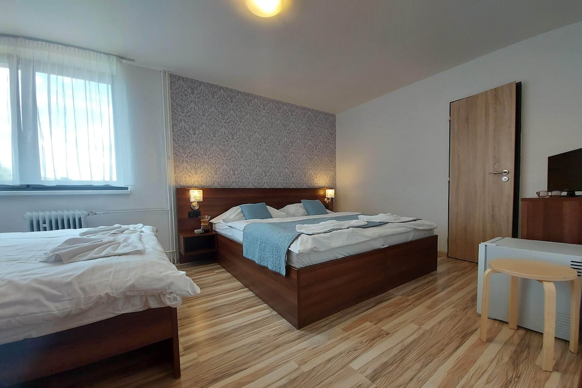 A hotel room with a double bed, a bedside table with a lamp, a wooden wardrobe, and a TV.