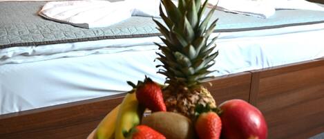 A hotel room with a neatly made bed, a bowl of fruit on a side table, and a patterned wallpaper on the wall.