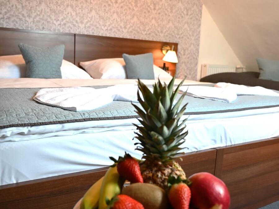 Una habitación de hotel con una cama bien hecha, un frutero sobre una mesita y un papel tapiz estampado en la pared.