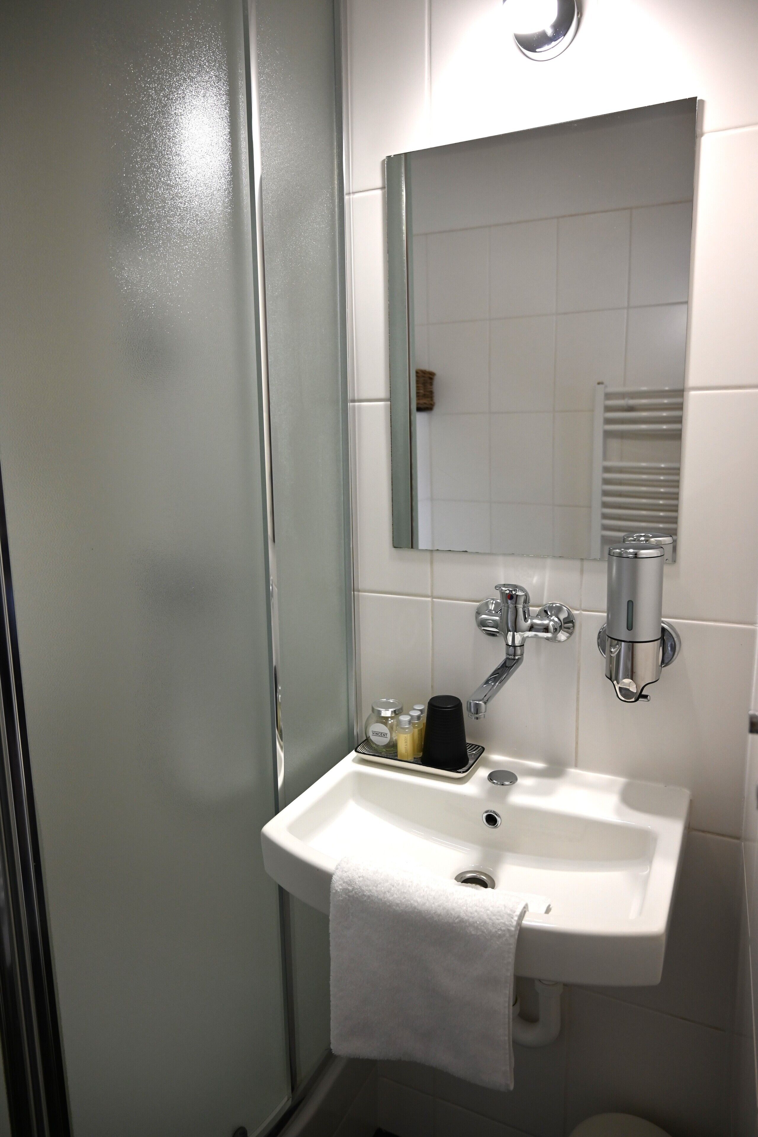 A bathroom with a glass shower door, a white sink with a towel, and a mirror above the sink.