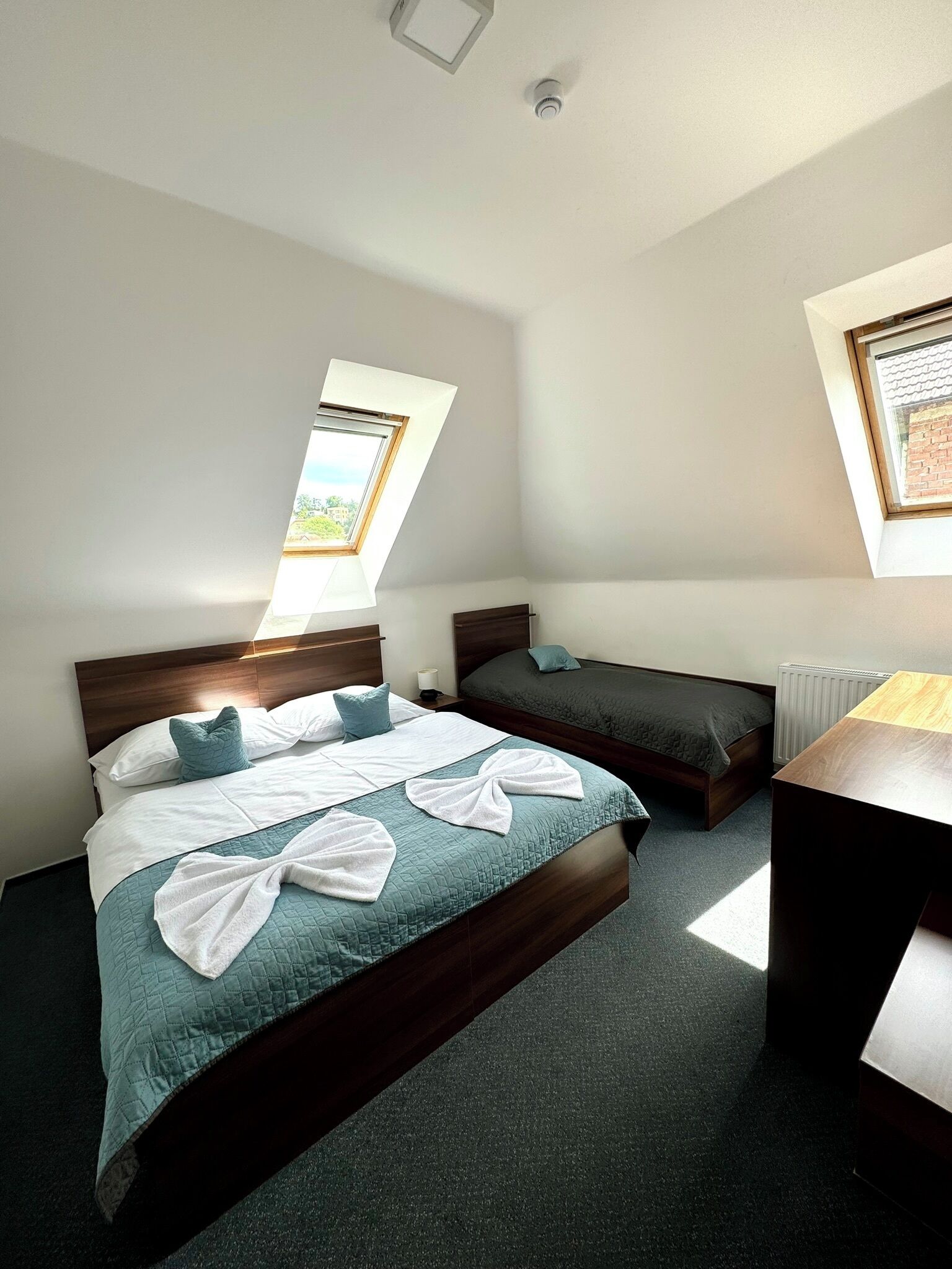 A modern hotel room with a large bed, a smaller bed, a desk, and a skylight.