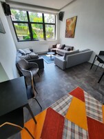 Una sala moderna con un sofá gris, una pequeña mesa redonda y una mesa de comedor negra. Una ventana grande ofrece vistas al exterior.