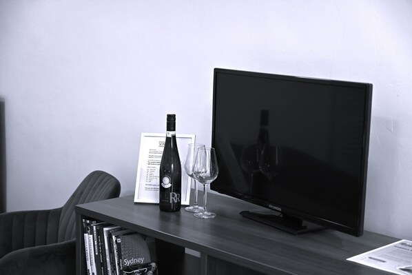 Un téléviseur posé sur un meuble, une bouteille de vin et deux verres à vin sur une table.