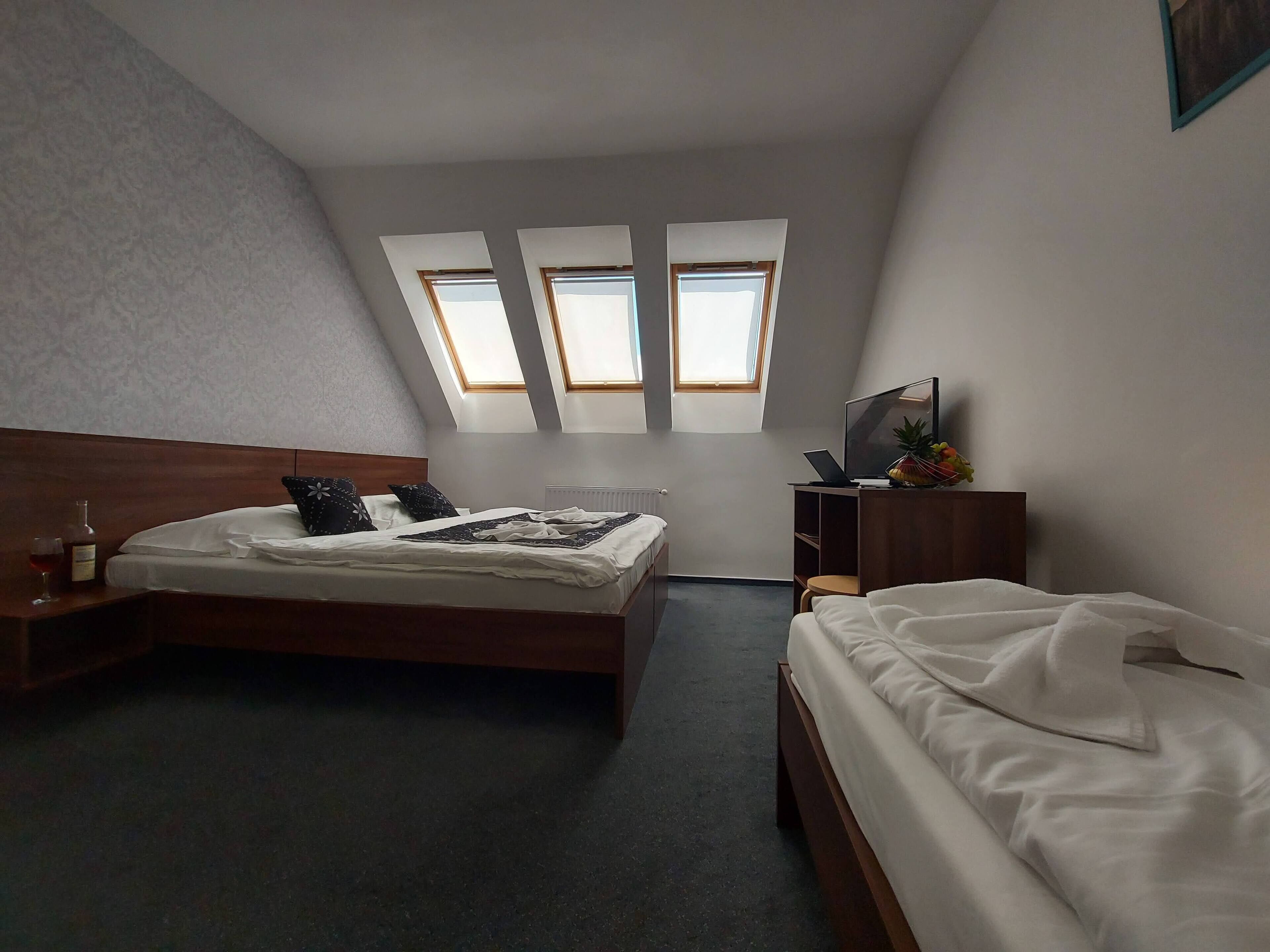A bedroom with a bed, a desk, a chair, a TV, and a window.