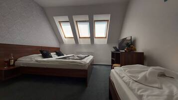 A bedroom with a bed, a desk, a chair, a TV, and a window.