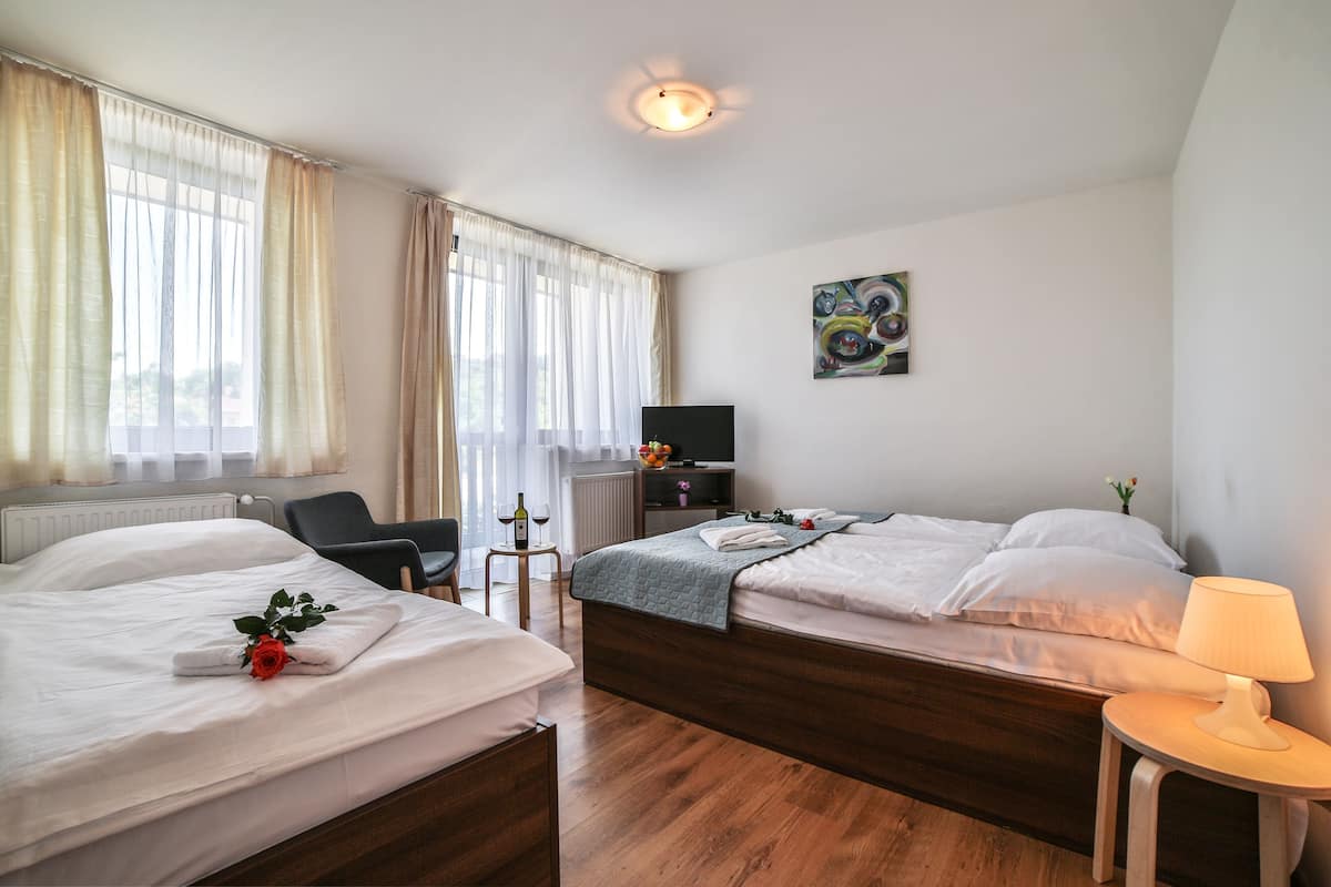 A hotel room with two beds, a desk, a chair, a TV, and a lamp.