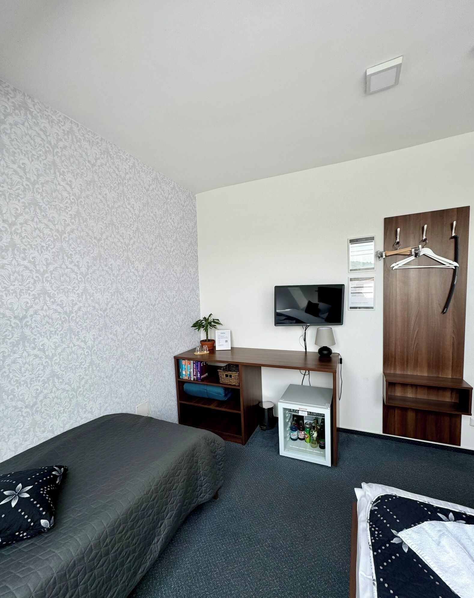 A bedroom with a bed, a desk with a TV, a wardrobe, and a small fridge.