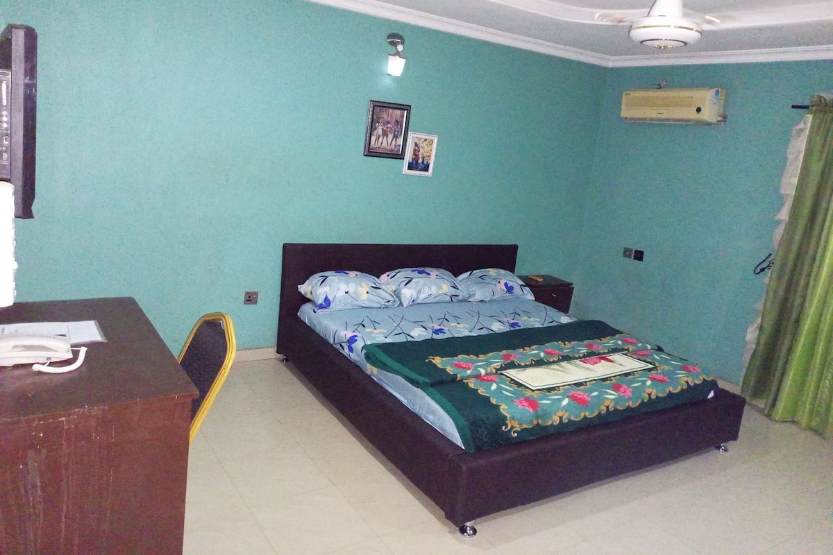 A bedroom with a bed, a desk, a chair, a ceiling fan, and a wall-mounted air conditioner.