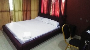 A single bed with white linens, a chair, and a desk with a chair. - De Villa Hotel and Suites (Badagry)