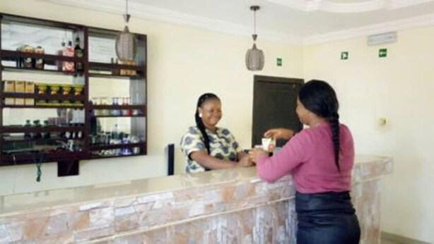 A reception area with a marble counter, a shelf with various items, and a door in the background. - De Villa Hotel and Suites (Badagry)