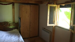 A bedroom with a wooden bed, a wardrobe, a radiator, and a window with a view of greenery.