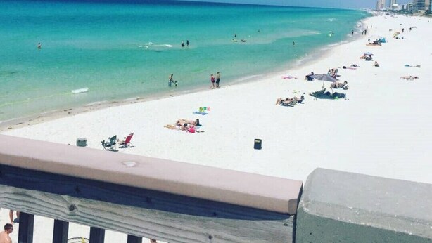 Une plage avec une eau turquoise et limpide, un rivage sablonneux et quelques bâtiments en arrière-plan.