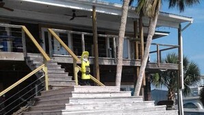 Un escalier en bois menant à un bâtiment à l’architecture moderne, avec des palmiers et un ciel dégagé.
