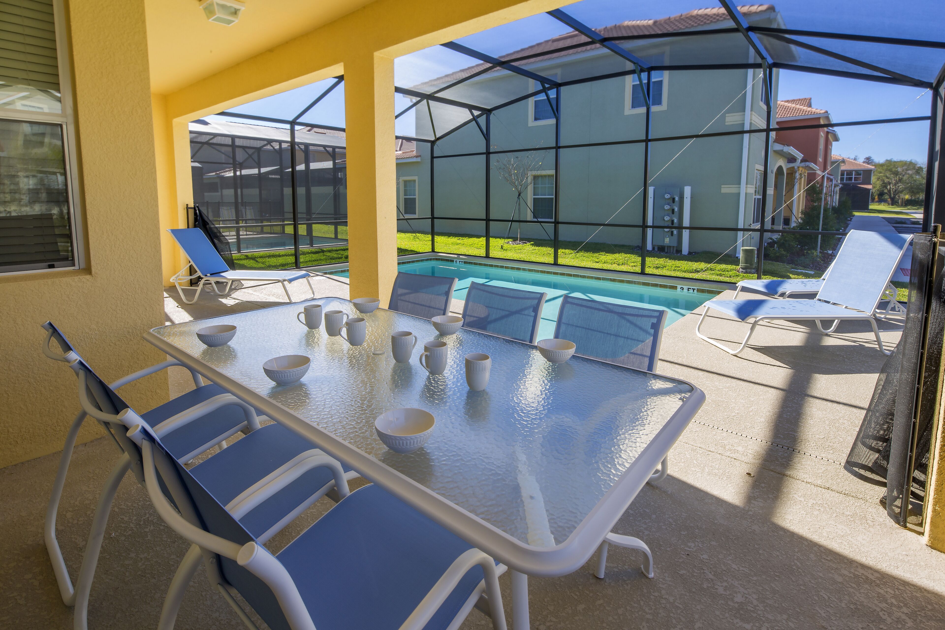 Un patio cubierto con una mesa y sillas de vidrio, con vista a una piscina y una casa.