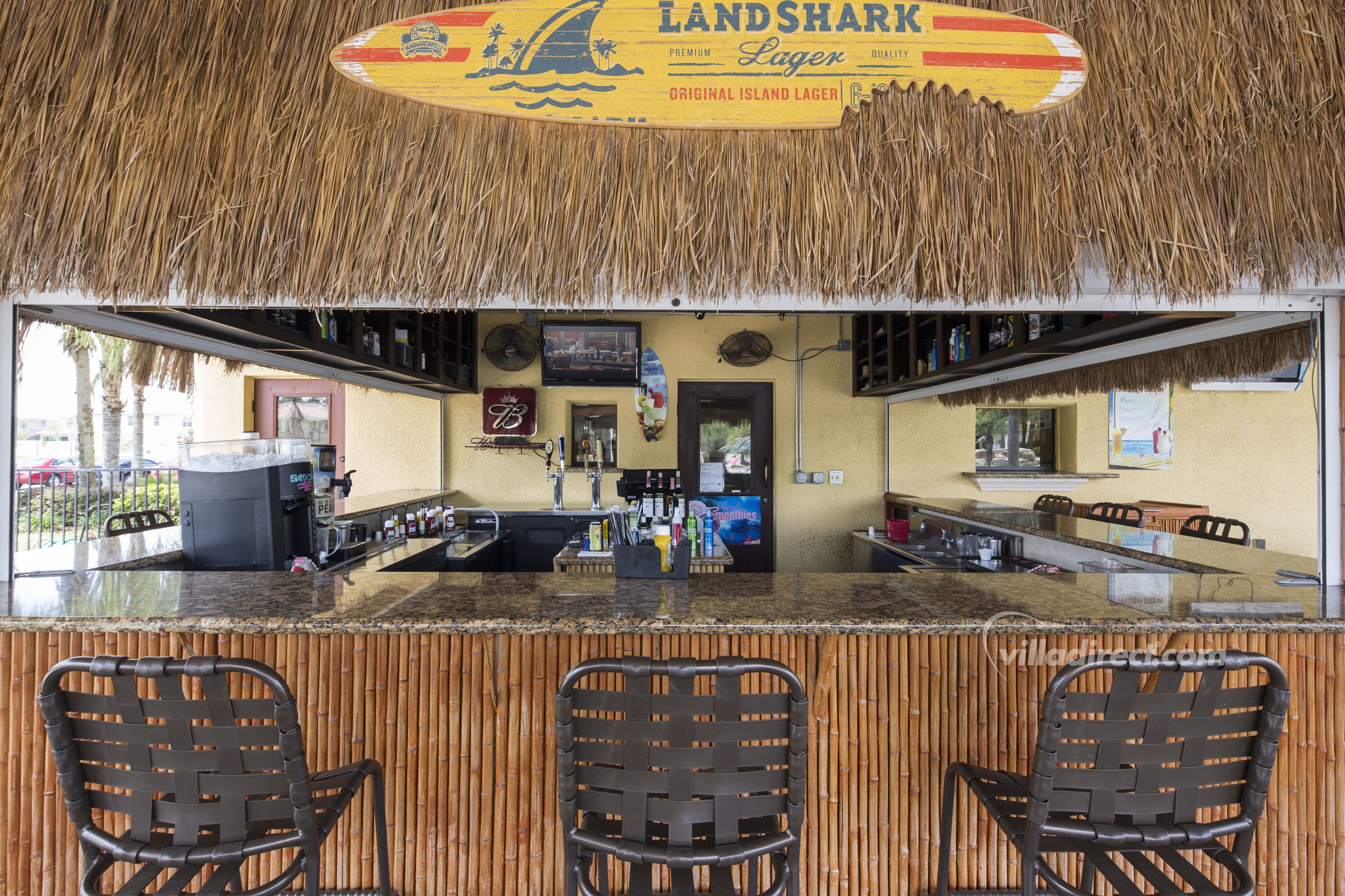 A bar with a thatched roof, a counter with stools, and a sign reading "Landshark Lager".