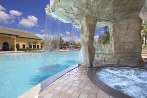 A pool with a waterfall feature, a hot tub, and a building with a tiled roof in the background. - Sun and Sand by VillaDirect (Kissimmee)