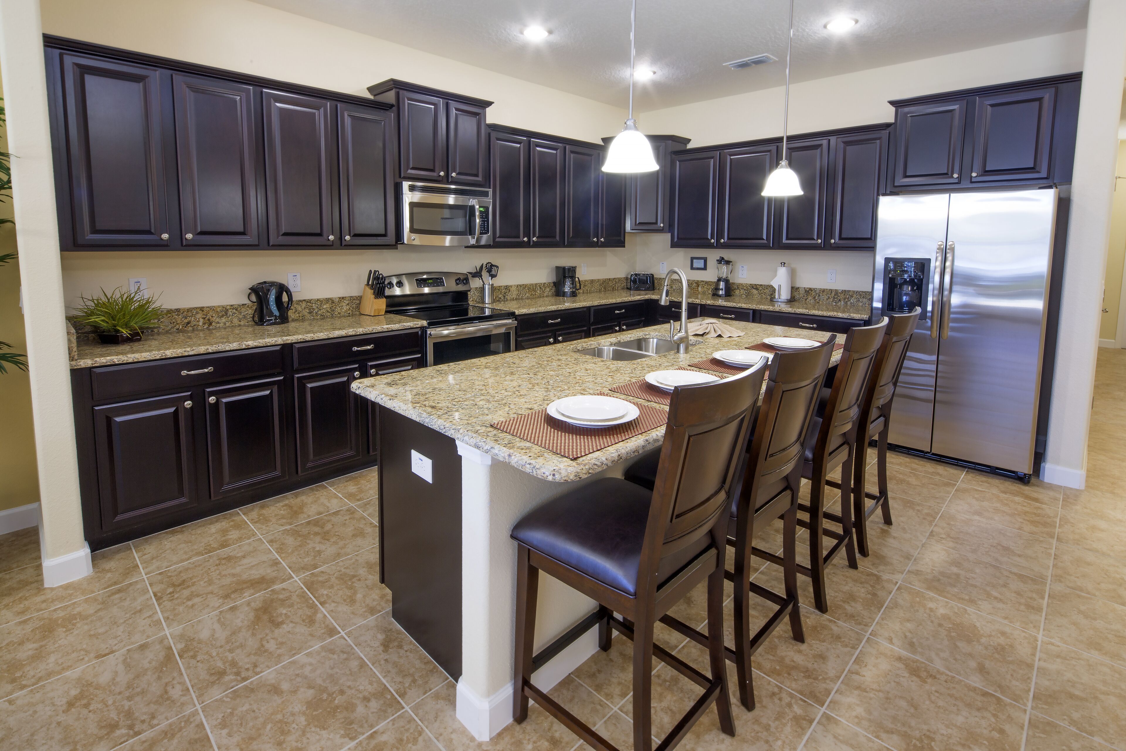 A modern kitchen with dark cabinets, stainless steel appliances, and a central island with bar stools.