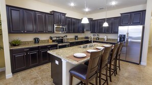 A modern kitchen with dark cabinets, stainless steel appliances, and a central island with bar stools.