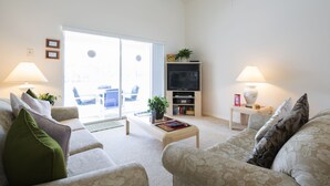 Un salon comprenant un canapé, une table basse, un téléviseur et des lampes. Une porte-fenêtre coulissante donne accès à un espace extérieur.