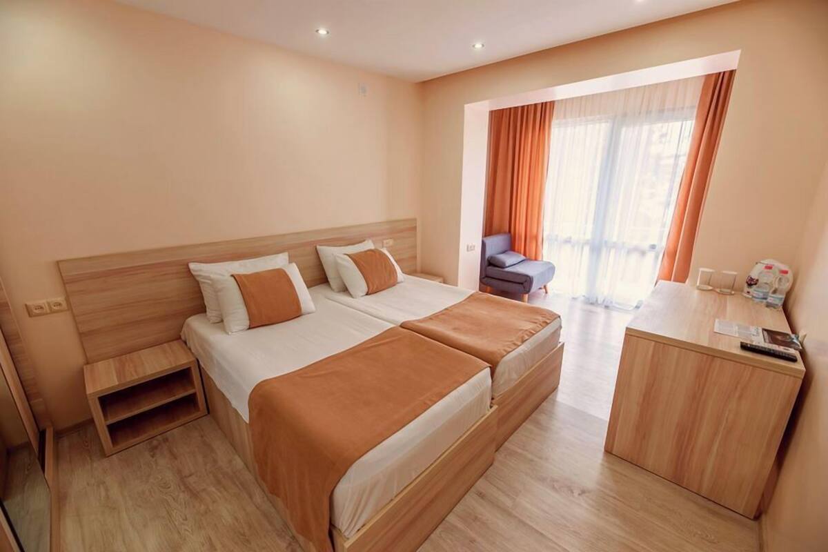 A hotel room with a double bed, a small desk, a chair, and a window with curtains.