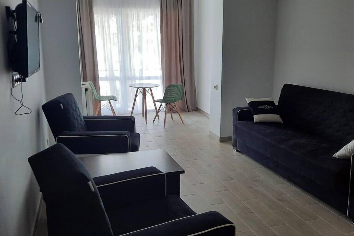 A modern living room with a sofa, two chairs, a small table, and a TV mounted on the wall.