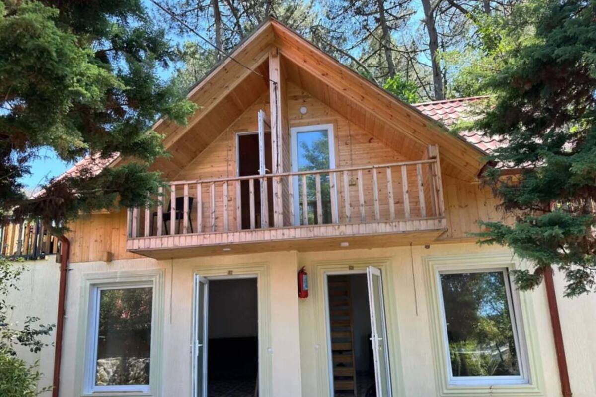 A wooden cabin with a balcony, a staircase, and a door leading to a garage.