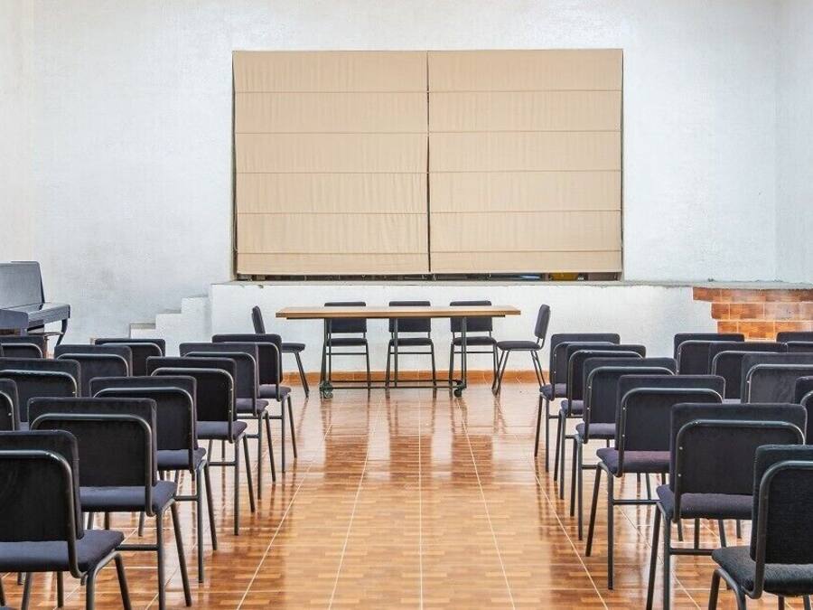 A conference room with rows of chairs, a large screen, and a piano.