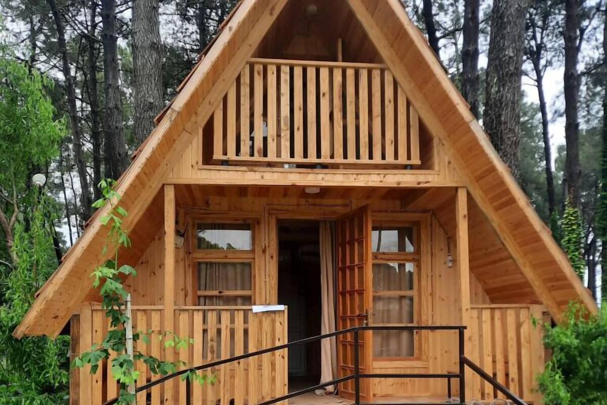 A wooden cabin with a balcony, stone foundation, and a wooden fence.