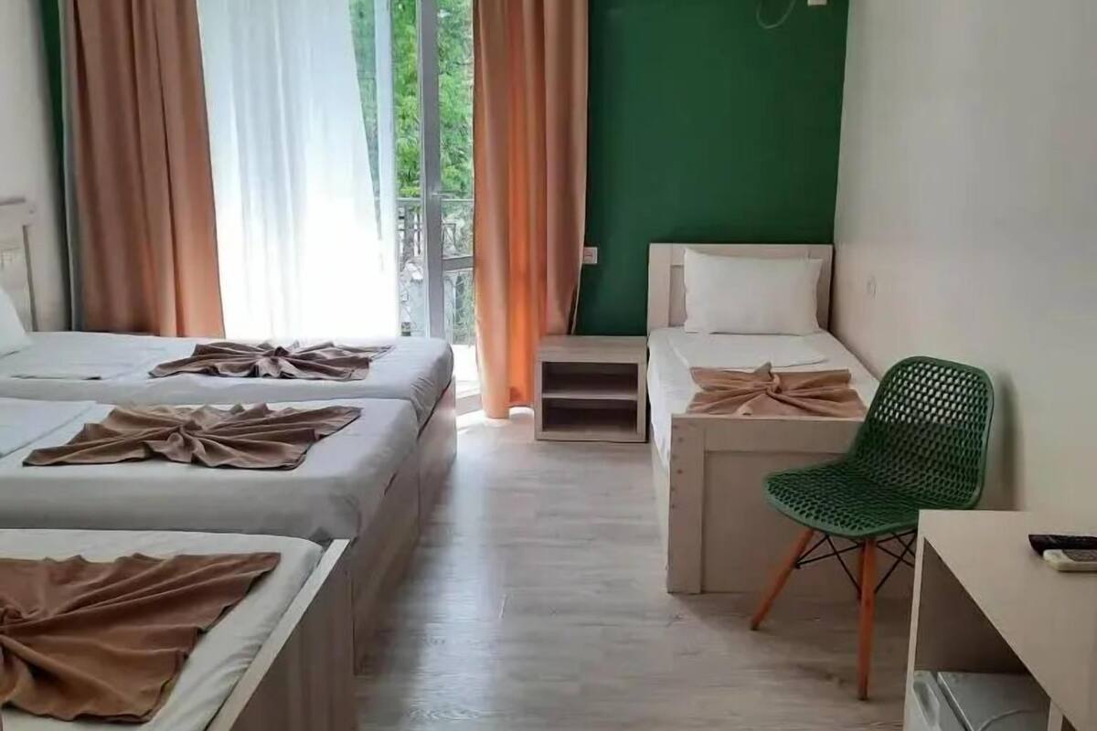 A hotel room with two beds, a desk, a chair, an air conditioning unit, and a balcony with curtains.