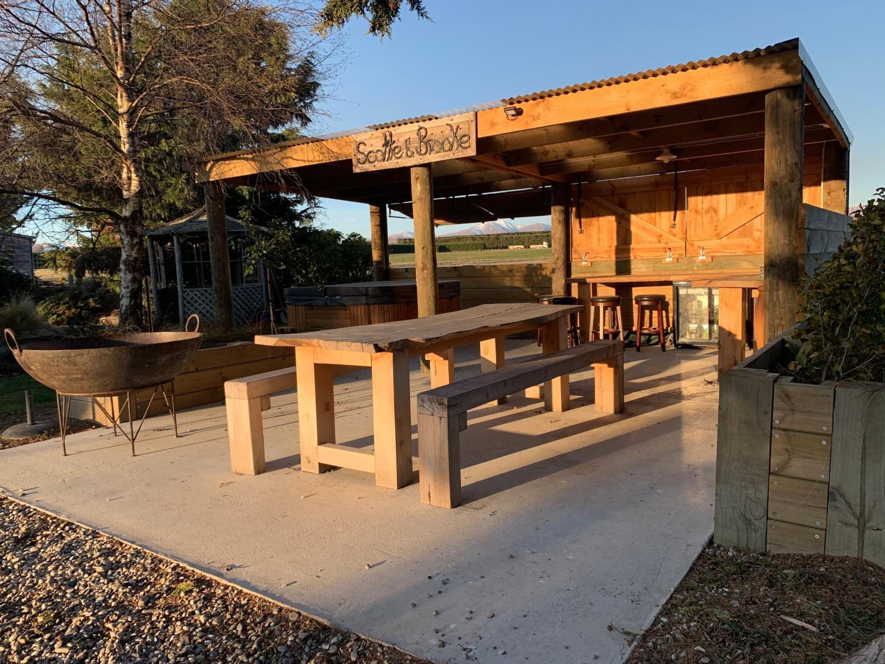 Une structure en bois installée à l’extérieur, sur laquelle est apposée une enseigne indiquant « Saddle & Broke », ainsi qu’un espace barbecue avec des tables et un gril.