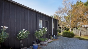 A rustic building with a dark wooden exterior, a gravel driveway, and potted plants including white roses. - Trout n Trail BnB (Ranfurly)
