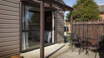 Un patio con una puerta corrediza de vidrio que da a una habitación, una valla de madera y mobiliario exterior.