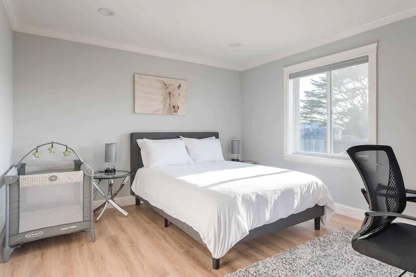 A bedroom with a bed, a crib, a chair, a window, and a painting on the wall.
