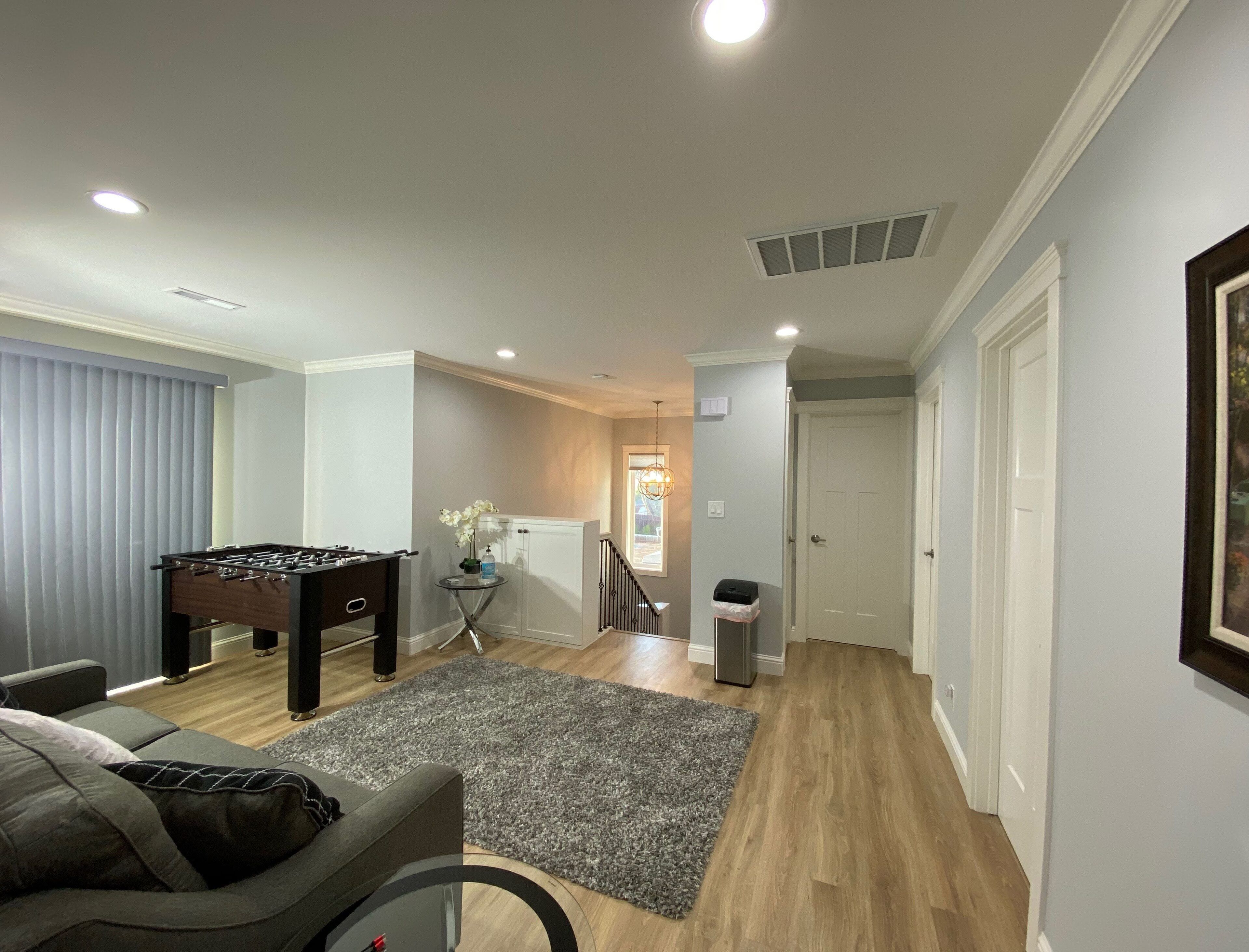 Ein modernes Wohnzimmer mit einem Kicker, einem grauen Sofa und Holzboden.