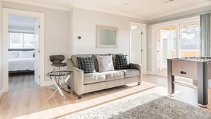 A modern living room with a sofa, a glass coffee table, and a foosball table. - Ocean-view 5BR near SF — sleeps 25 (Pacifica)