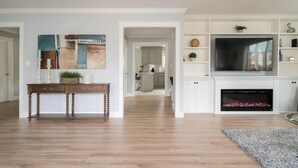 A modern living room with hardwood flooring, a fireplace, a TV, and a dining area with a wooden table and chairs. - Ocean-view 5BR near SF — sleeps 25 (Pacifica)