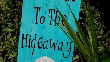 Een houten bord met de tekst 'Welcome To The Hideaway', omringd door groen.
