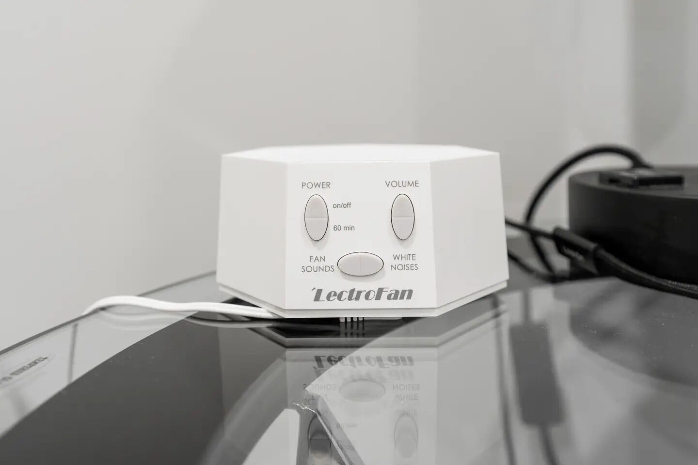 Un dispositivo 'LectroFan' blanco sobre una superficie reflectante, con controles para encendido, volumen, sonidos de ventilador y ruidos blancos.